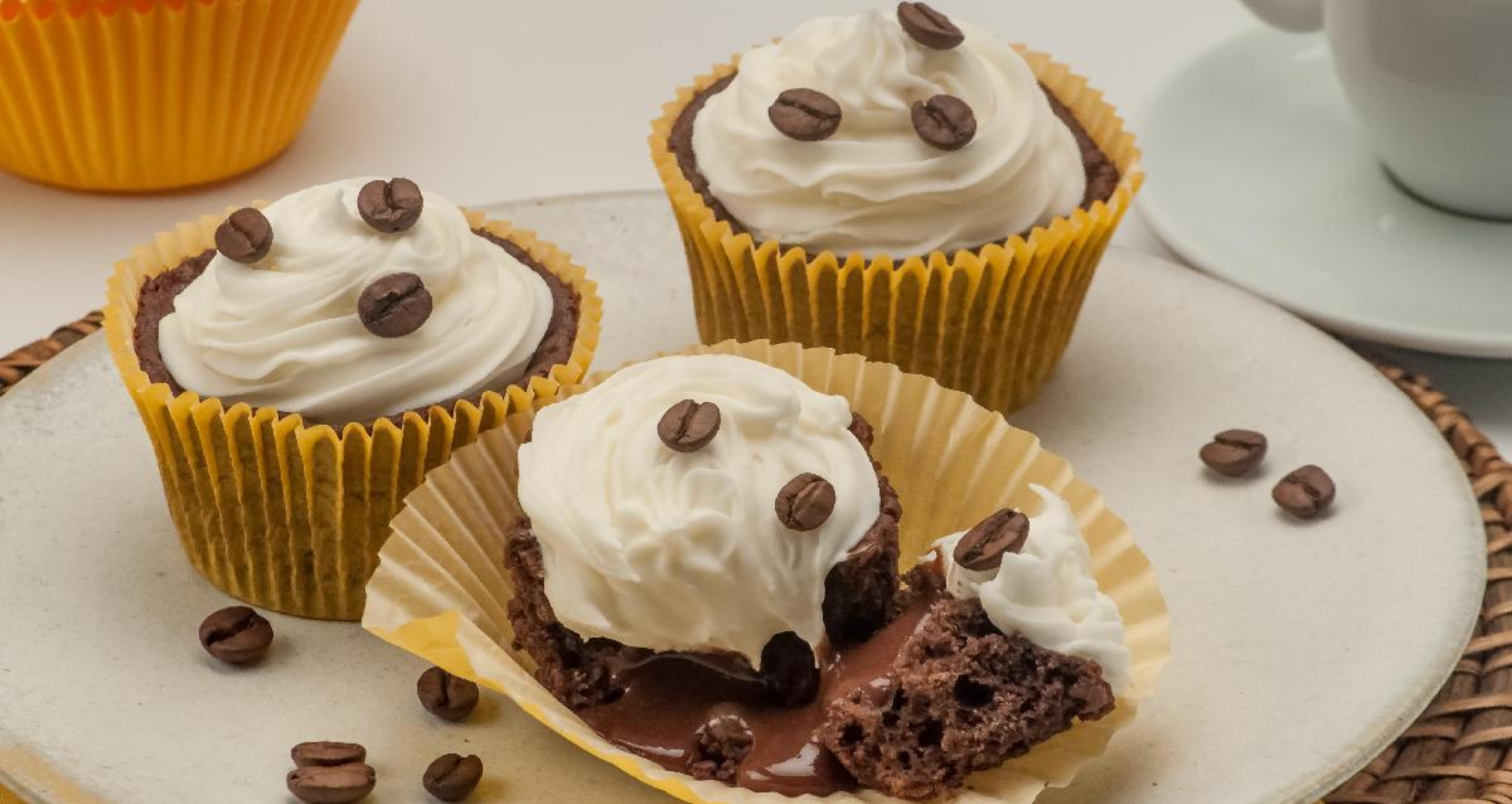 Imagem apresenta três cupcakes de café, com grãos de café e chantilly